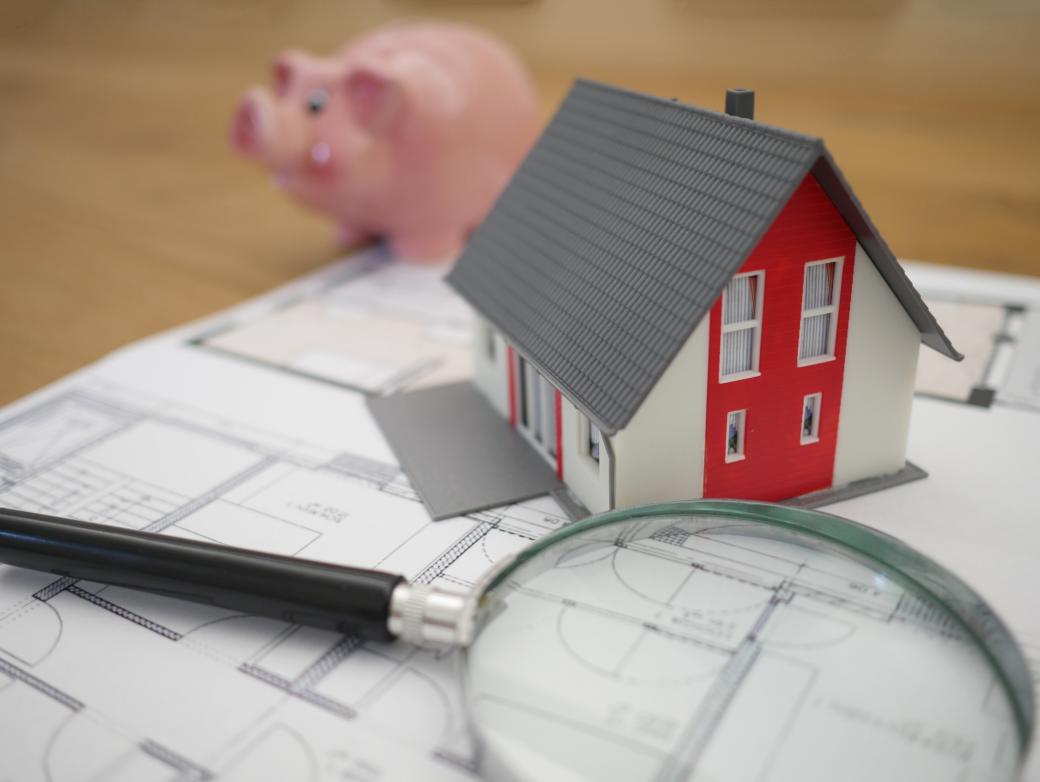 Eine Lupe und ein Modellhaus liegen auf einem Bauplan