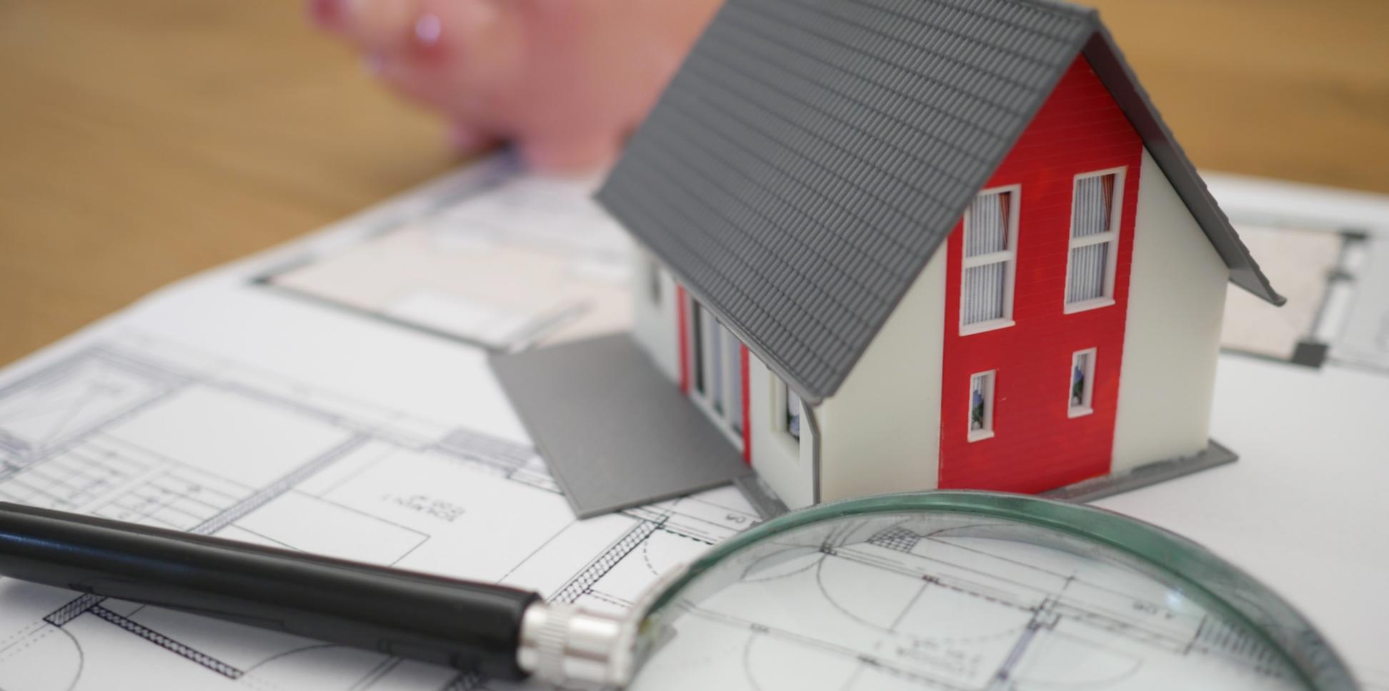 Eine Lupe und ein Modellhaus liegen auf einem Bauplan