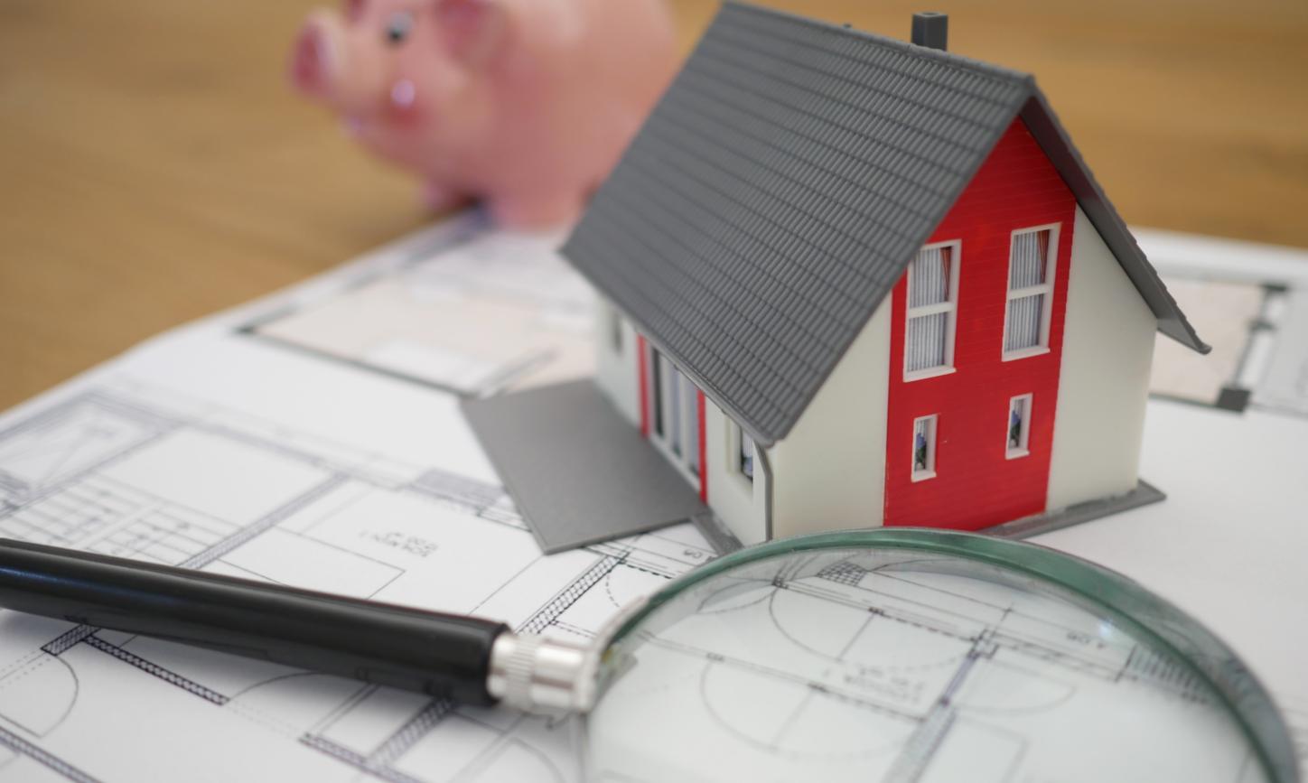 Eine Lupe und ein Modellhaus liegen auf einem Bauplan